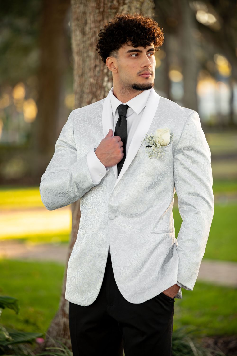 A formal white tuxedo jacket with black details is showcased in an outdoor portrait session.