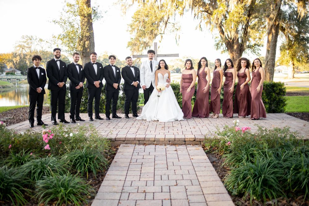 Wedding party members in formal attire pose together on a stone patio surrounded by greenery.
