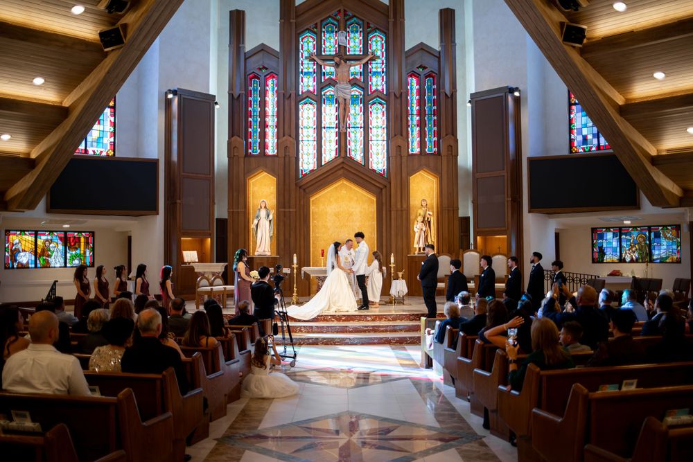 A wedding ceremony in progress inside a beautiful church with stained glass windows and wooden beams.