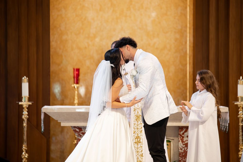 A couple stands at the altar during a traditional Catholic wedding ceremony in a church with golden walls.