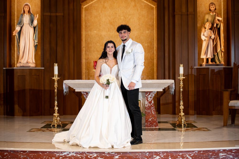A couple poses for romantic wedding photos inside a grand church with ornate wooden details and golden candelabras.