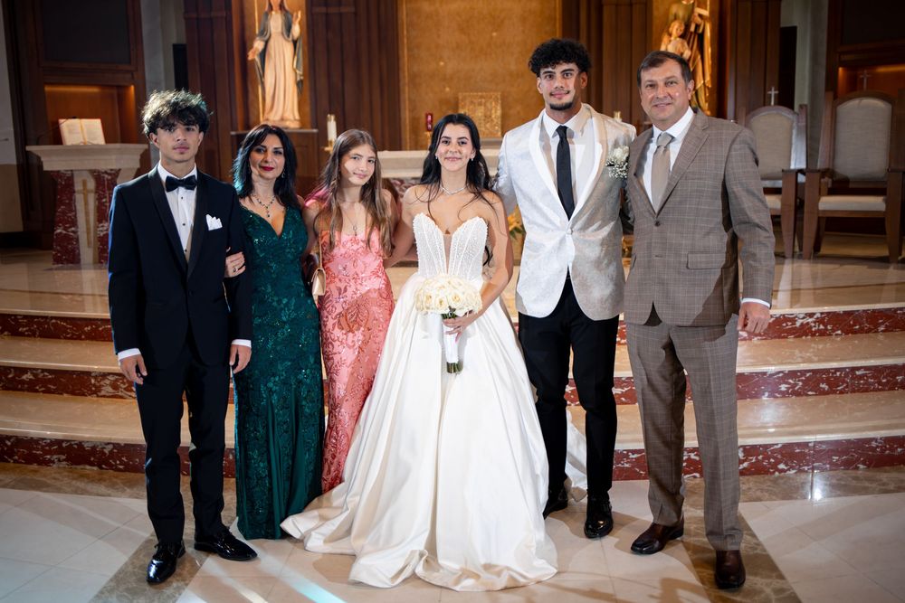 A wedding party poses together inside an ornate church with marble columns and decorative altar in the background.