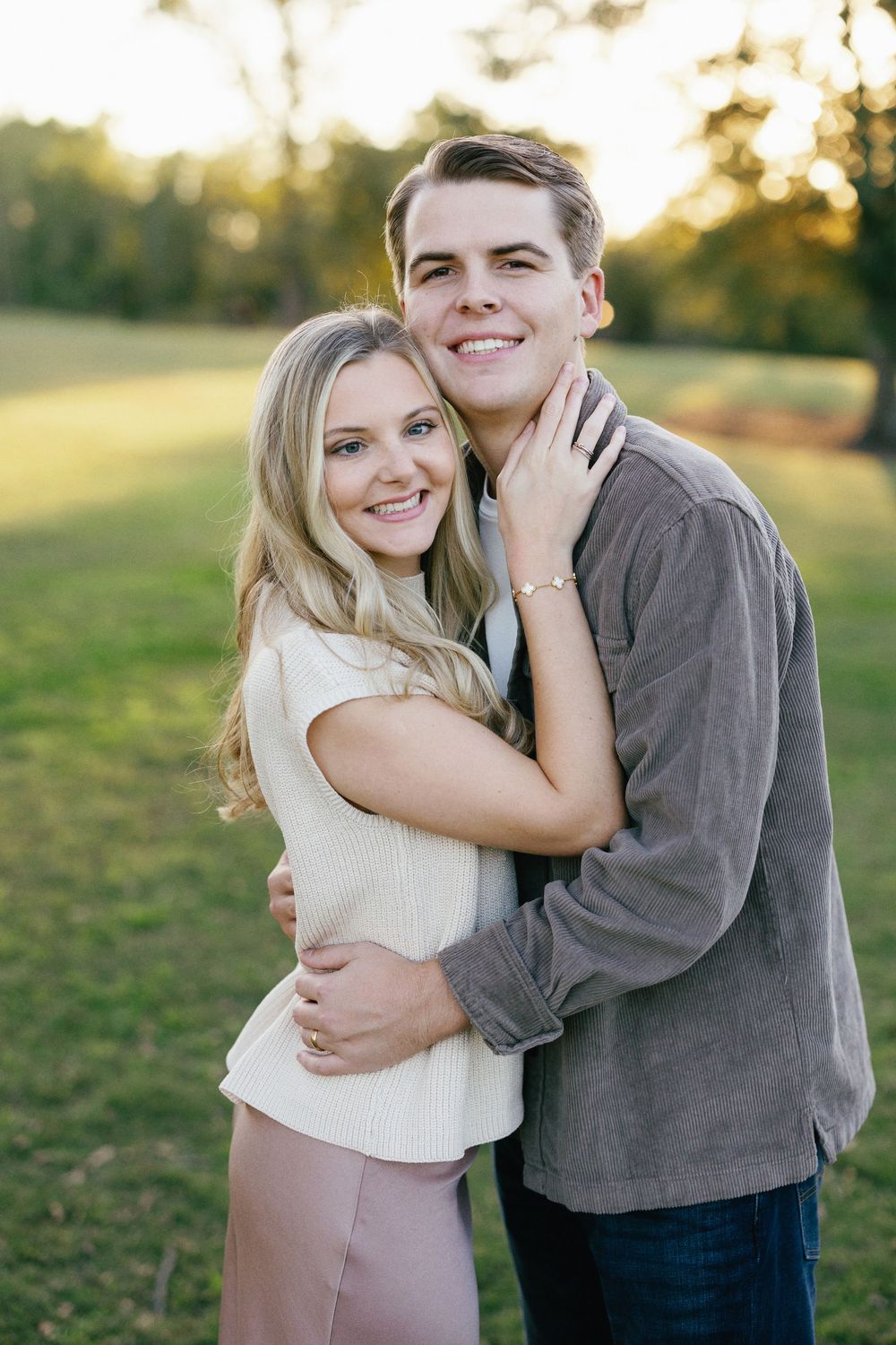 A couple embraces and smiles together during a romantic outdoor photoshoot at golden hour.