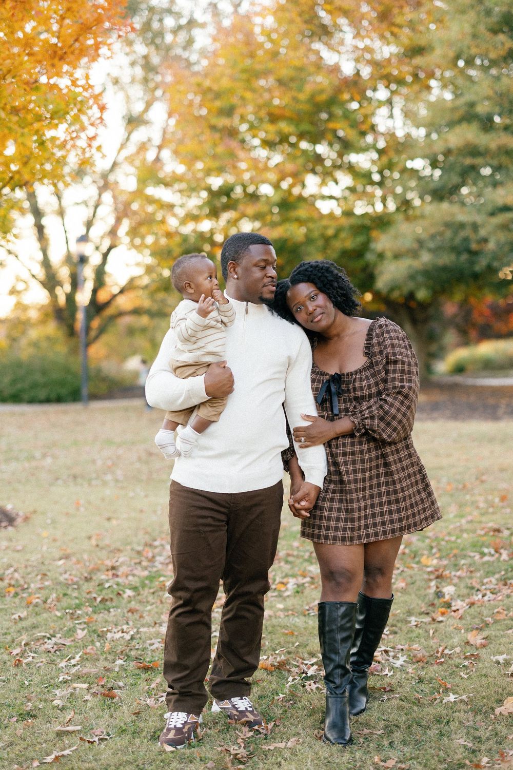 A couple shares playful laughter together during an autumn photoshoot in a park with golden fall foliage.
