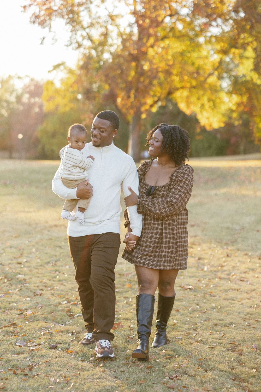 A family walks together through a sun-drenched autumn field with golden leaves and warm lighting.