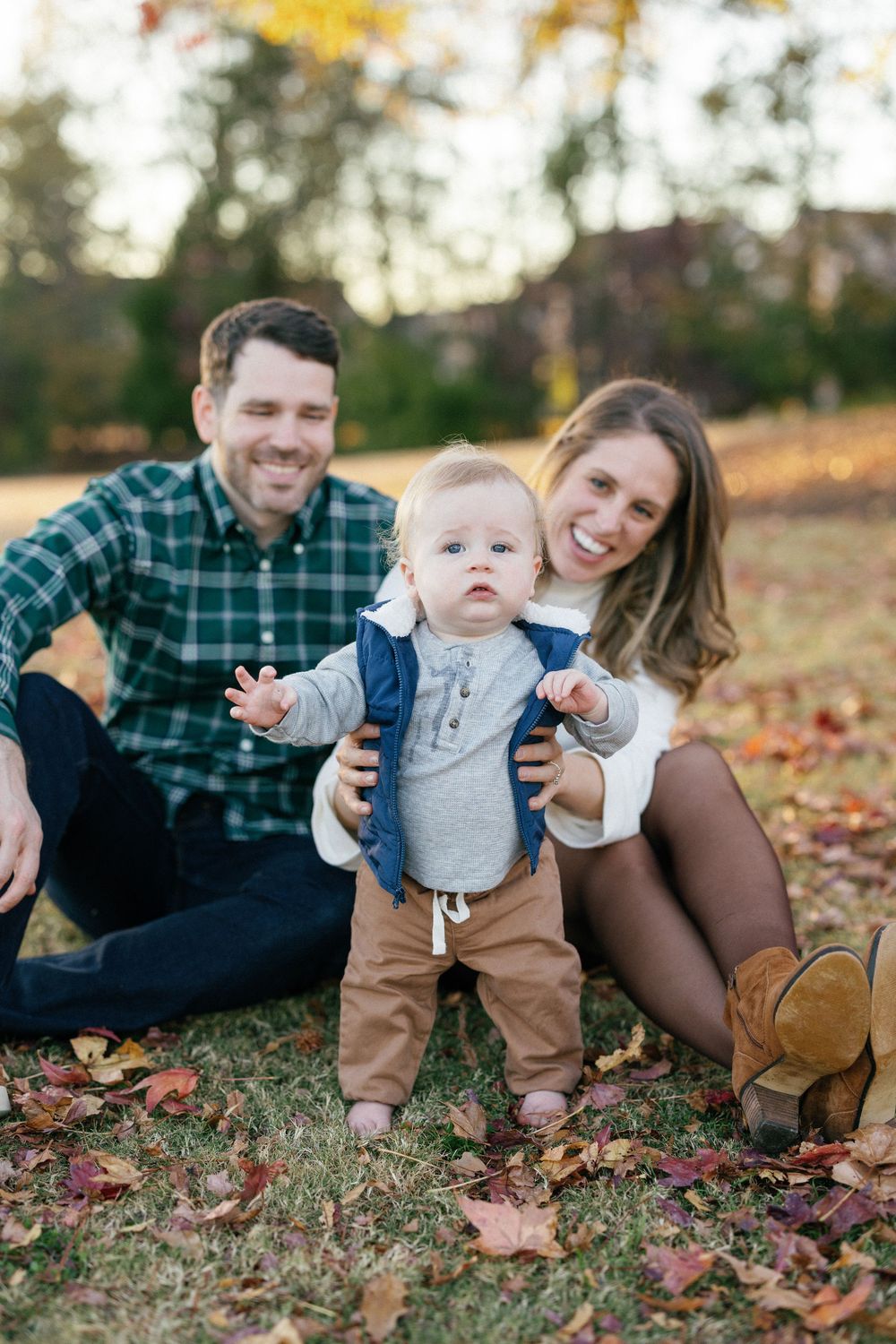 A family sits together on autumn leaves during an outdoor photo session in warm evening light.