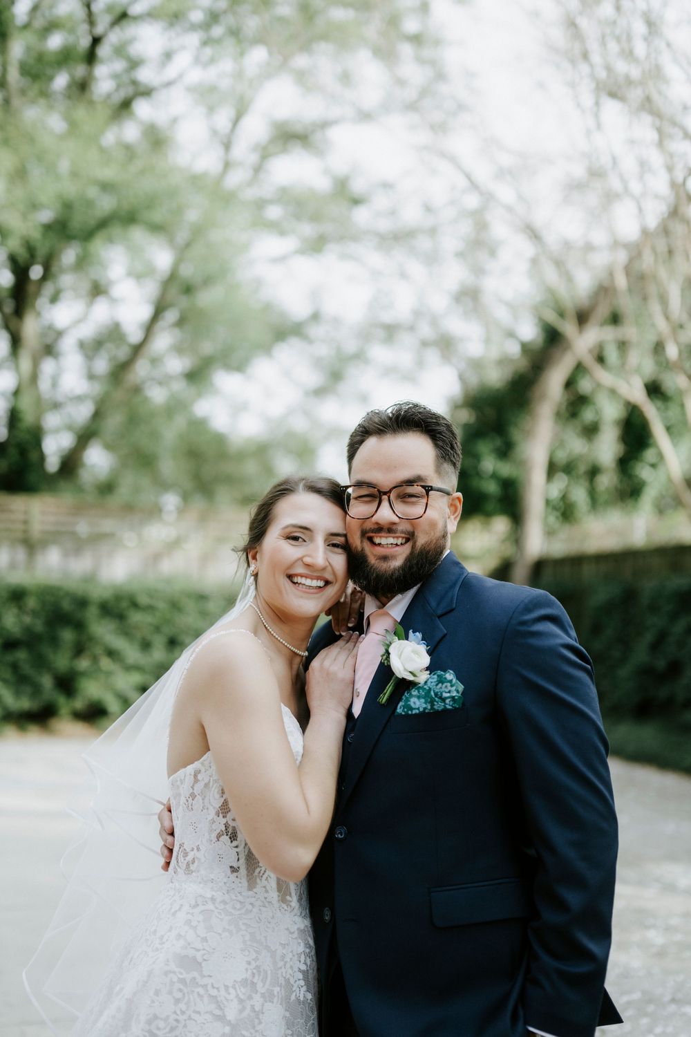 A romantic wedding photoshoot outdoors with a couple embracing in formal attire against a blurred natural background.