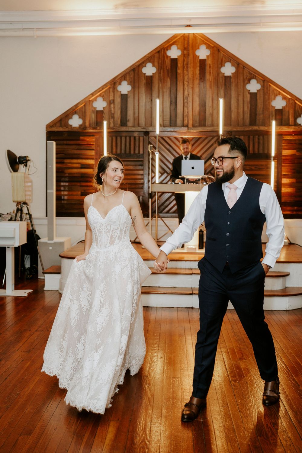 Dancing couple in wedding attire twirl and embrace on a rustic wooden dance floor with warm lighting.