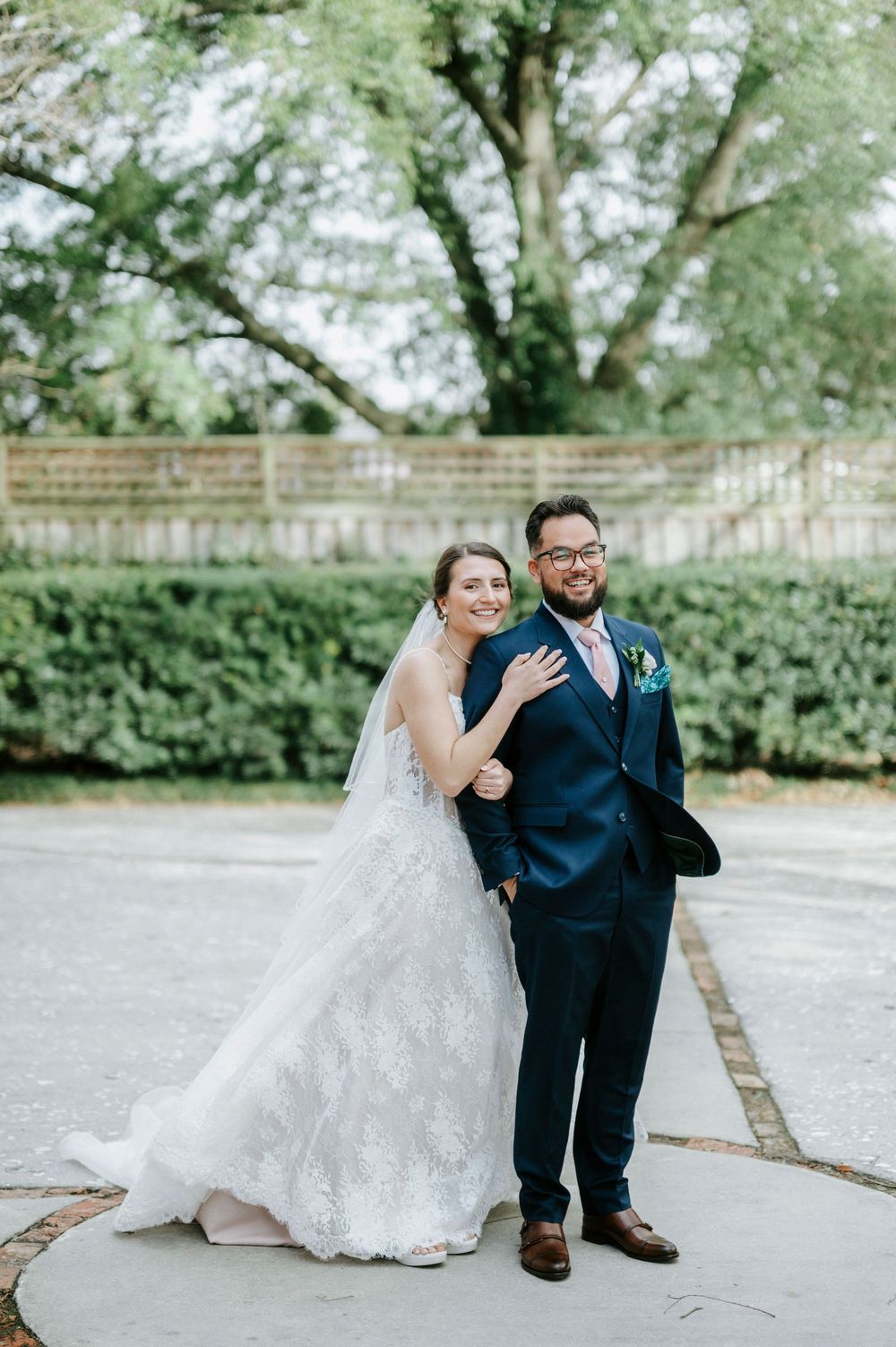 A couple poses for a wedding portrait outdoors with lush greenery and trees in the background.
