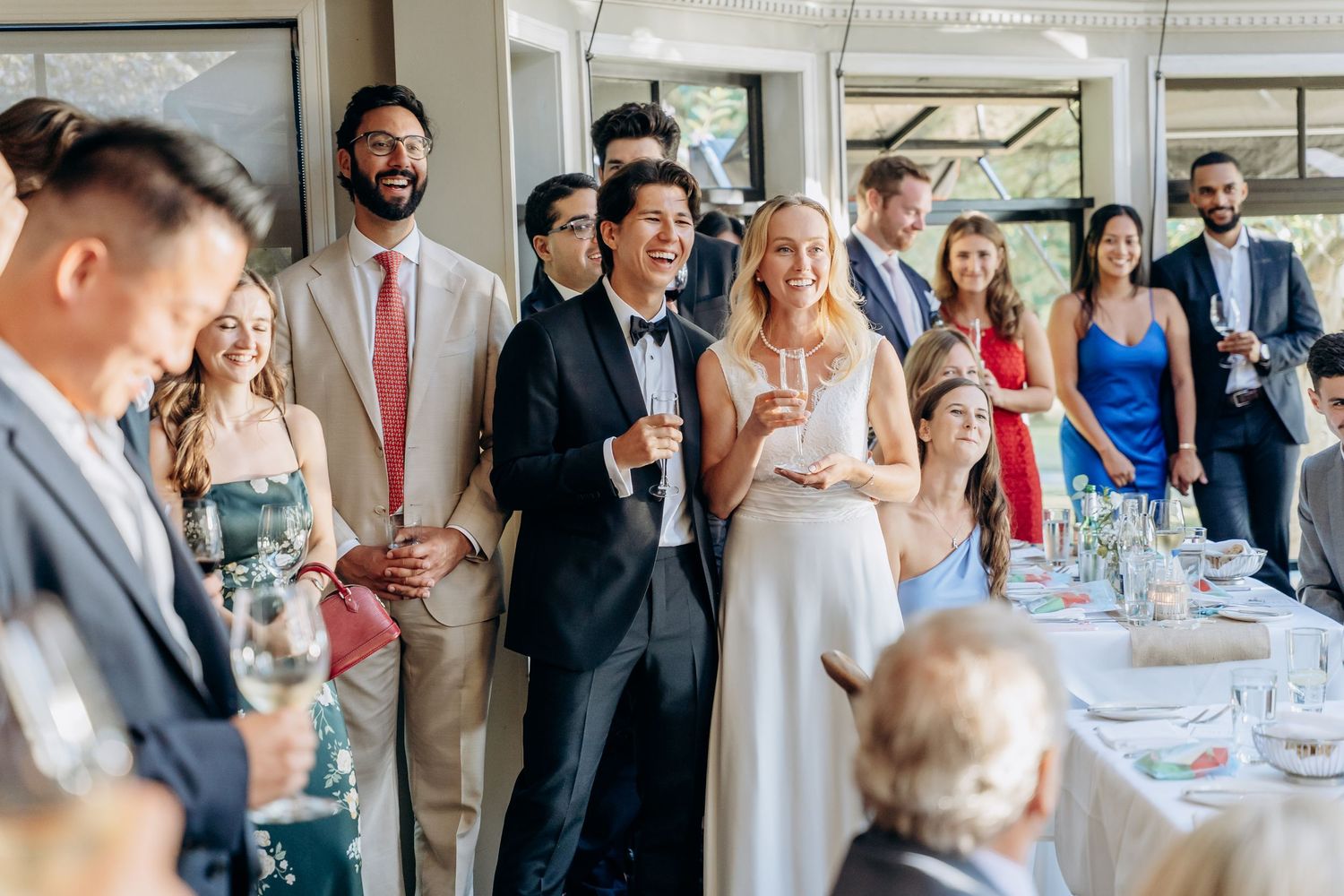 Wedding guests raise champagne glasses during an elegant reception toast at an indoor venue.