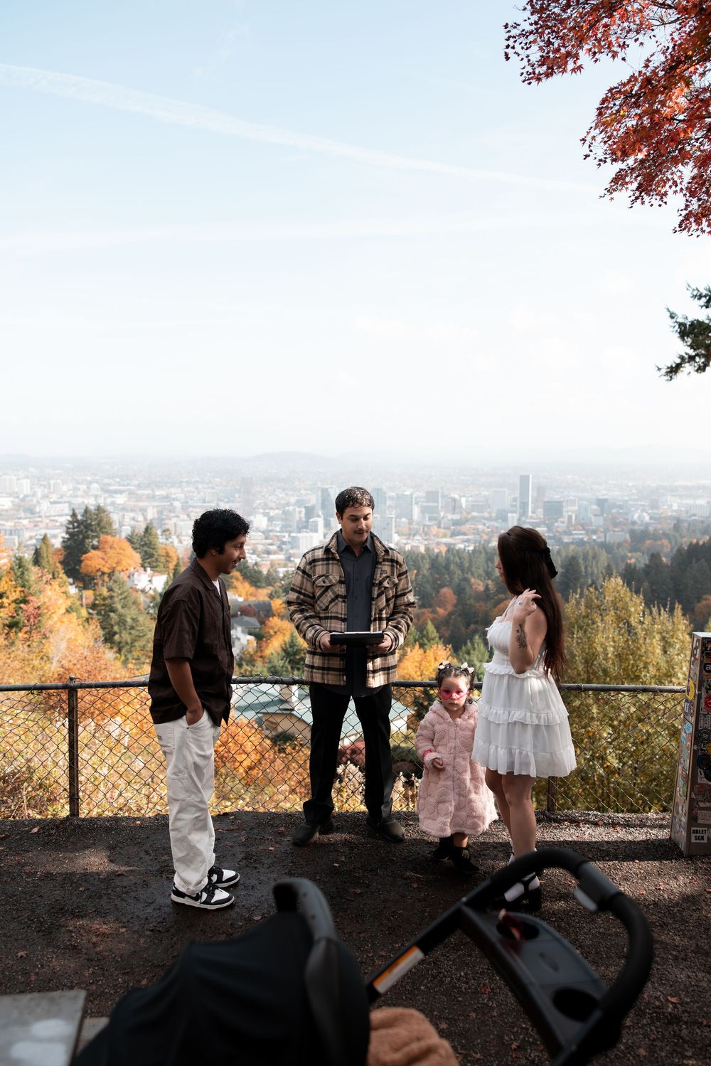 A group gathers at a scenic overlook with autumn foliage and city views in the background during golden hour.