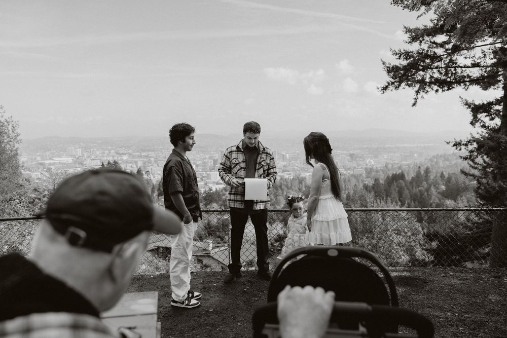 A black and white outdoor ceremony takes place on a scenic overlook with mountains visible in the background.