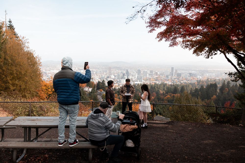 Visitors gather at a scenic viewpoint overlooking Portland Oregon on a misty autumn day with fall foliage.