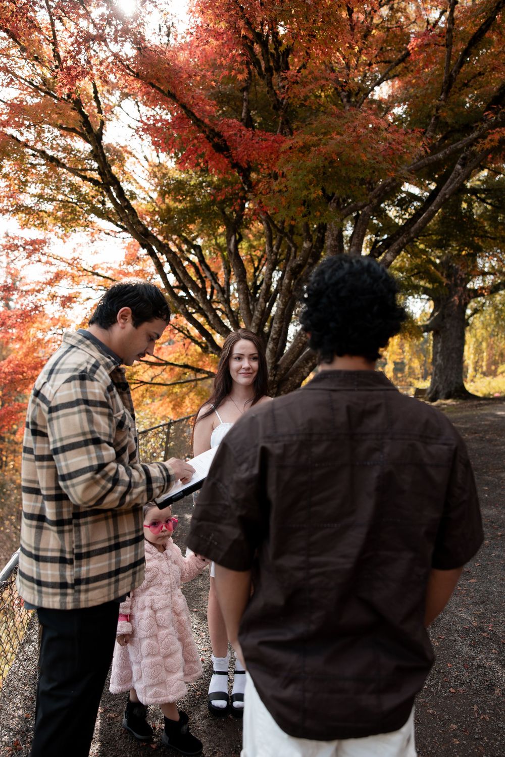A couple shares an intimate moment under vibrant autumn maple trees with red and orange foliage.