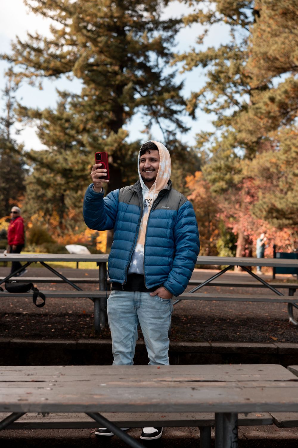 Person in a blue puffer jacket and light pants stands on a wooden deck during autumn.