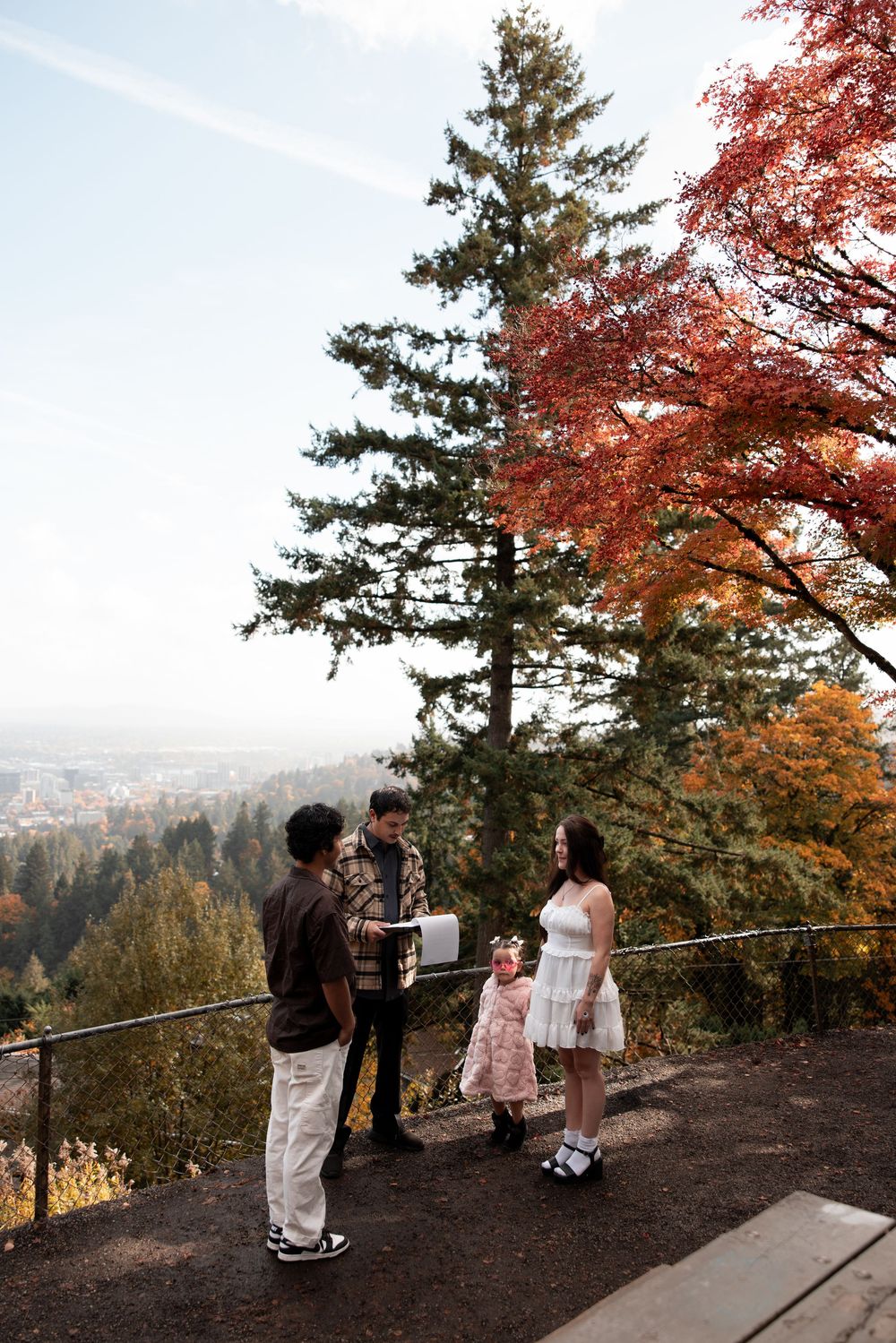 Group of people gather at a scenic mountain viewpoint surrounded by fall foliage and evergreen trees.