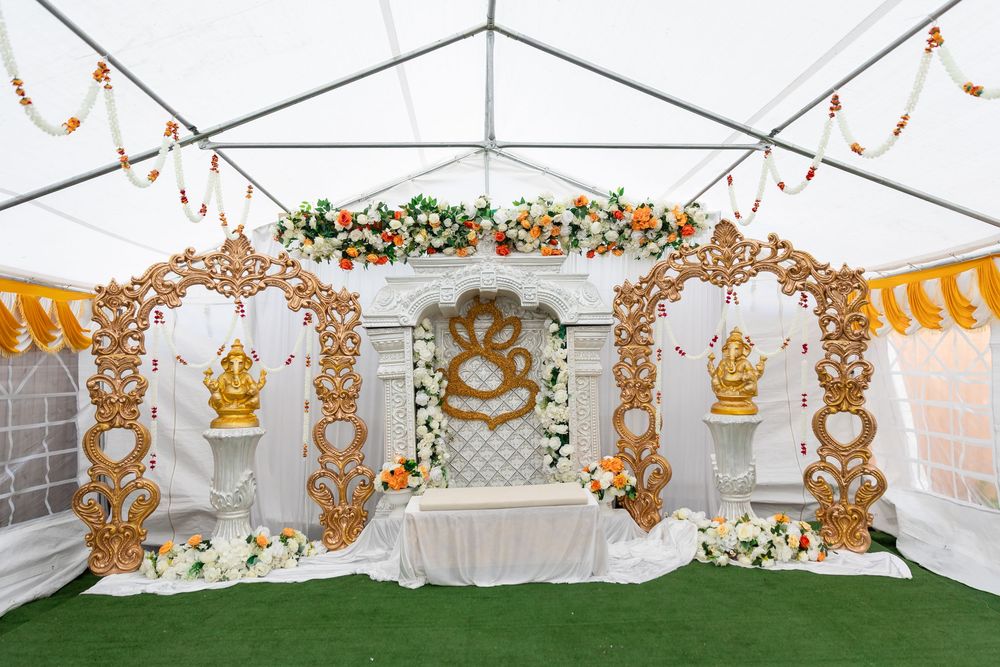 Elegant white wedding backdrop with ornate gold accents and floral arrangements in a white tent setting.