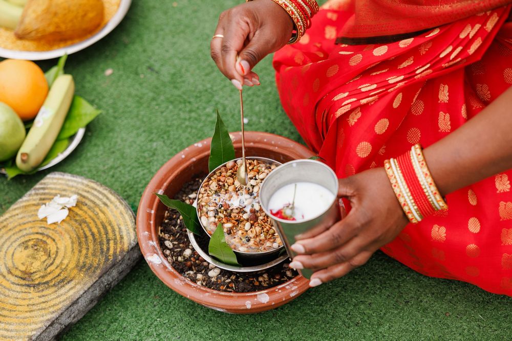 Hands in red traditional attire preparing Indian tea with spices and ingredients on a green textured surface.