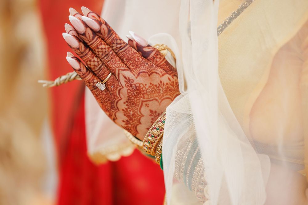 Traditional Indian wedding ceremony with bride and groom exchanging rings in ornate decor with gold accents.