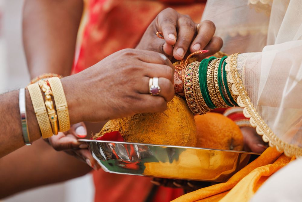 Close-up of hands with bangles and jewelry performing traditional Indian wedding ritual with yellow spices.