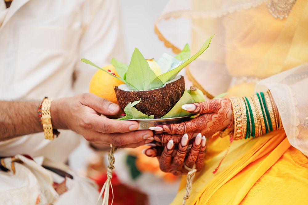 Hands holding a decorated coconut with green leaves during a traditional Hindu wedding ritual ceremony.