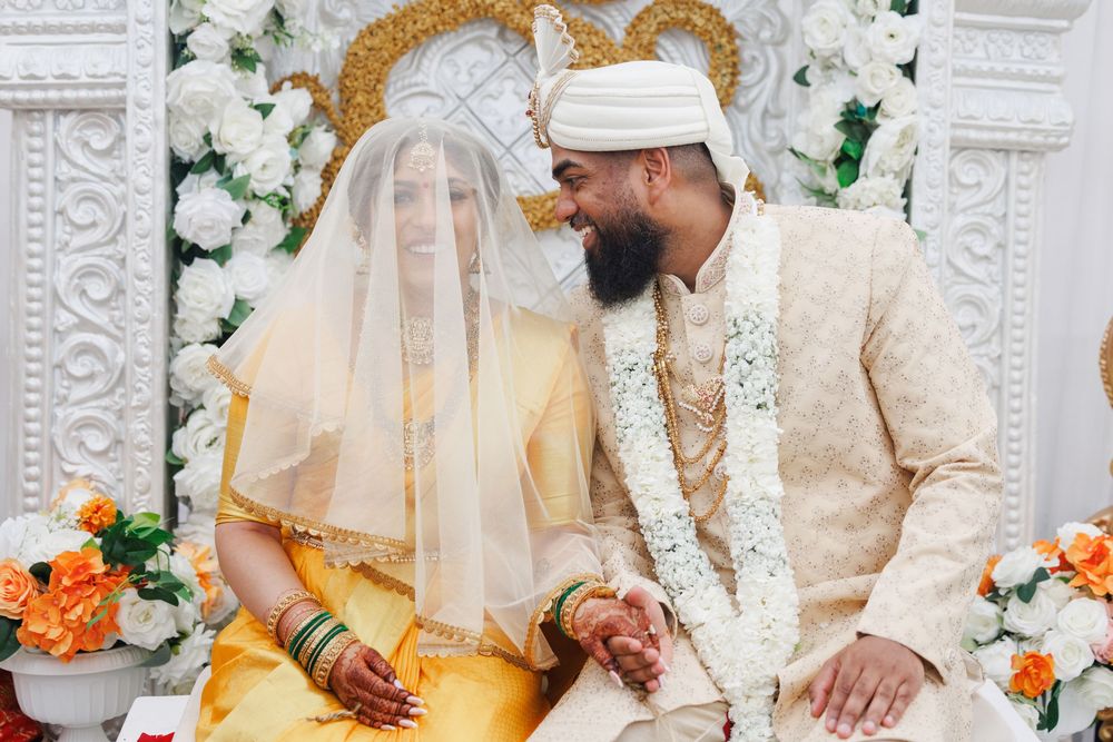 Wedding couple performs traditional Hindu marriage rituals with floral and gold decorative backdrop.