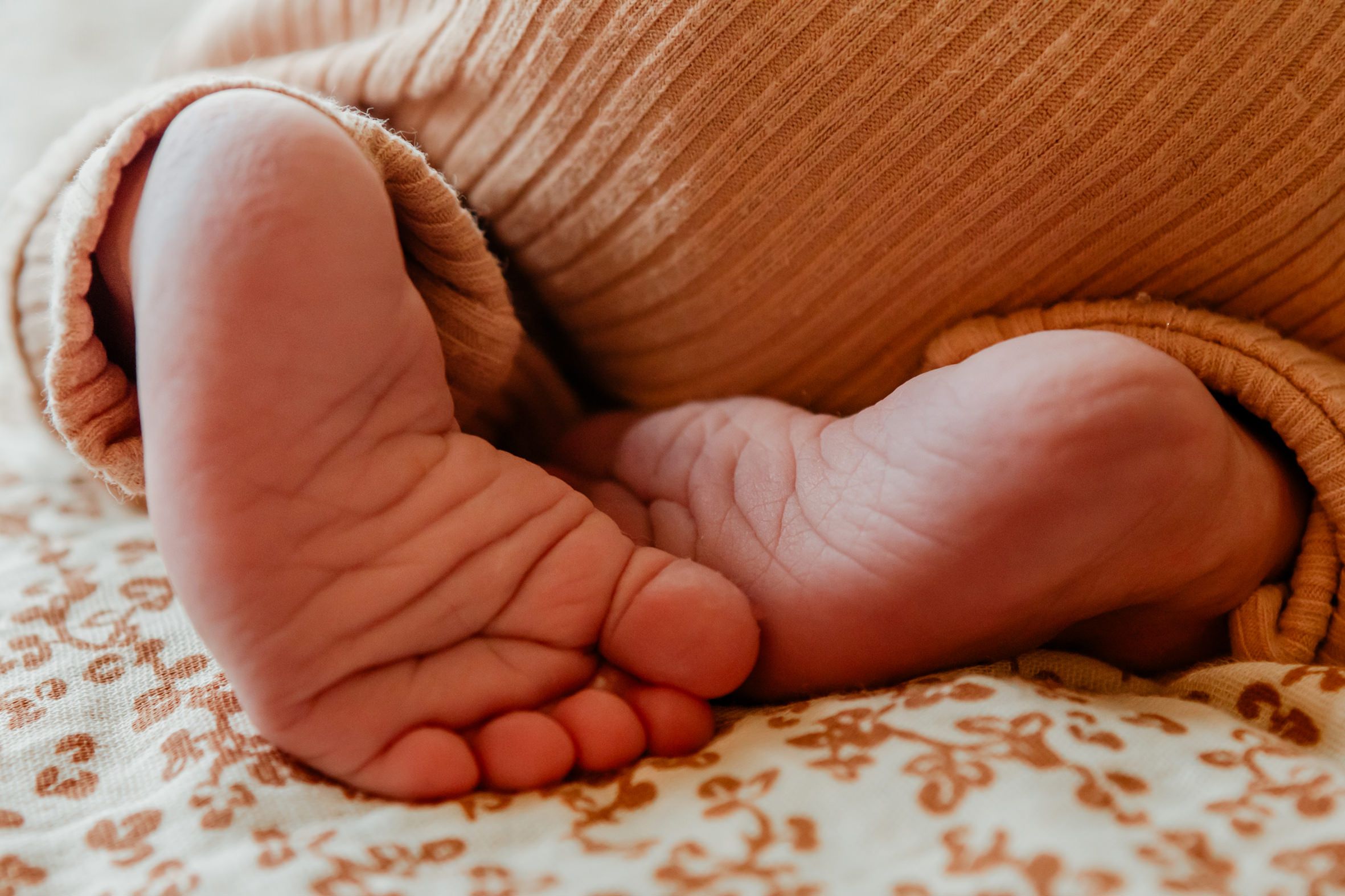 Close-up van babyvoetjes tijdens een lifestyle newbornshoot, met een oranje rompertje en opgetrokken beentjes