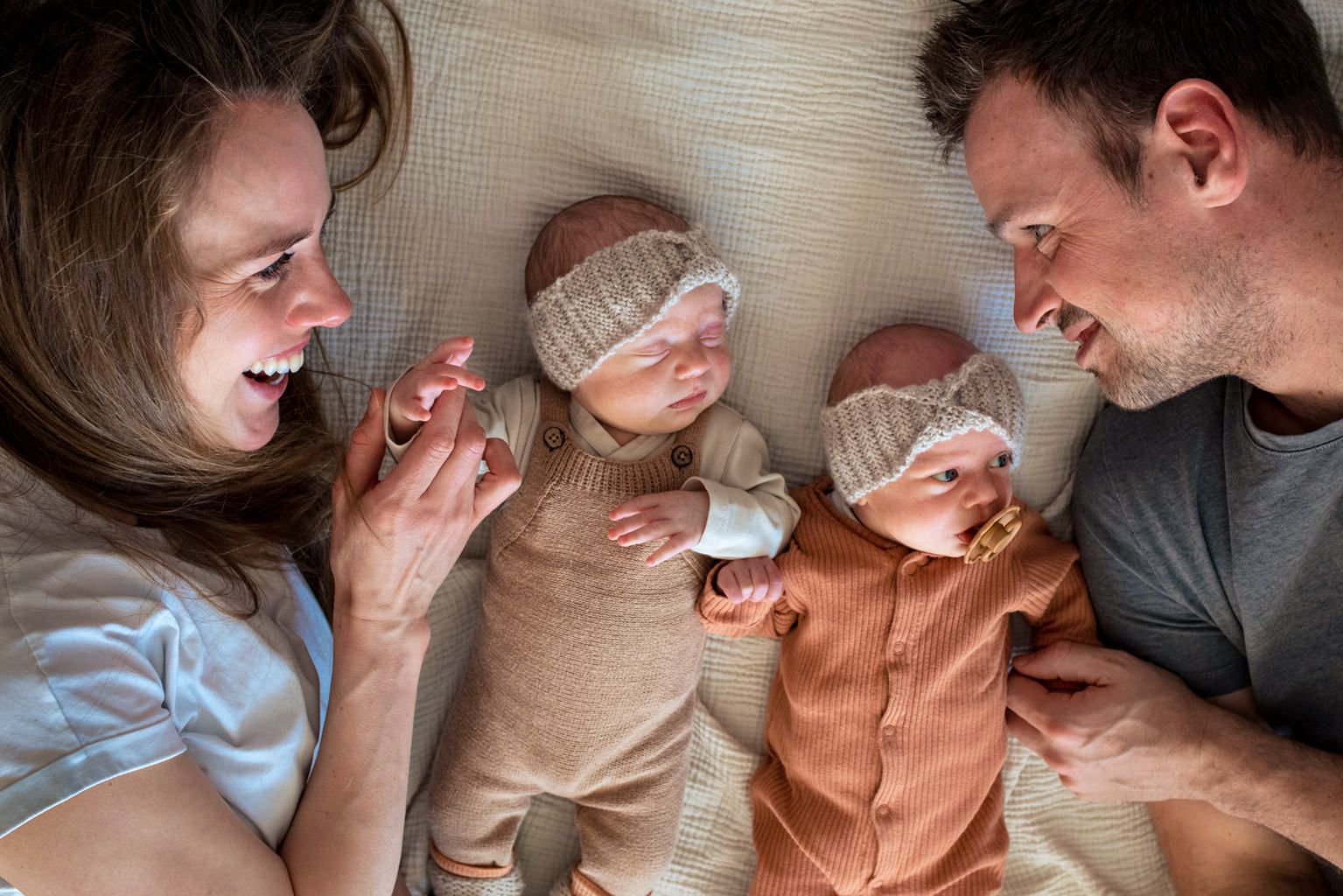 Ouders samen met hun tweeling meisjes tijdens een lifestyle newbornshoot, met haarbandjes en liefdevolle interactie