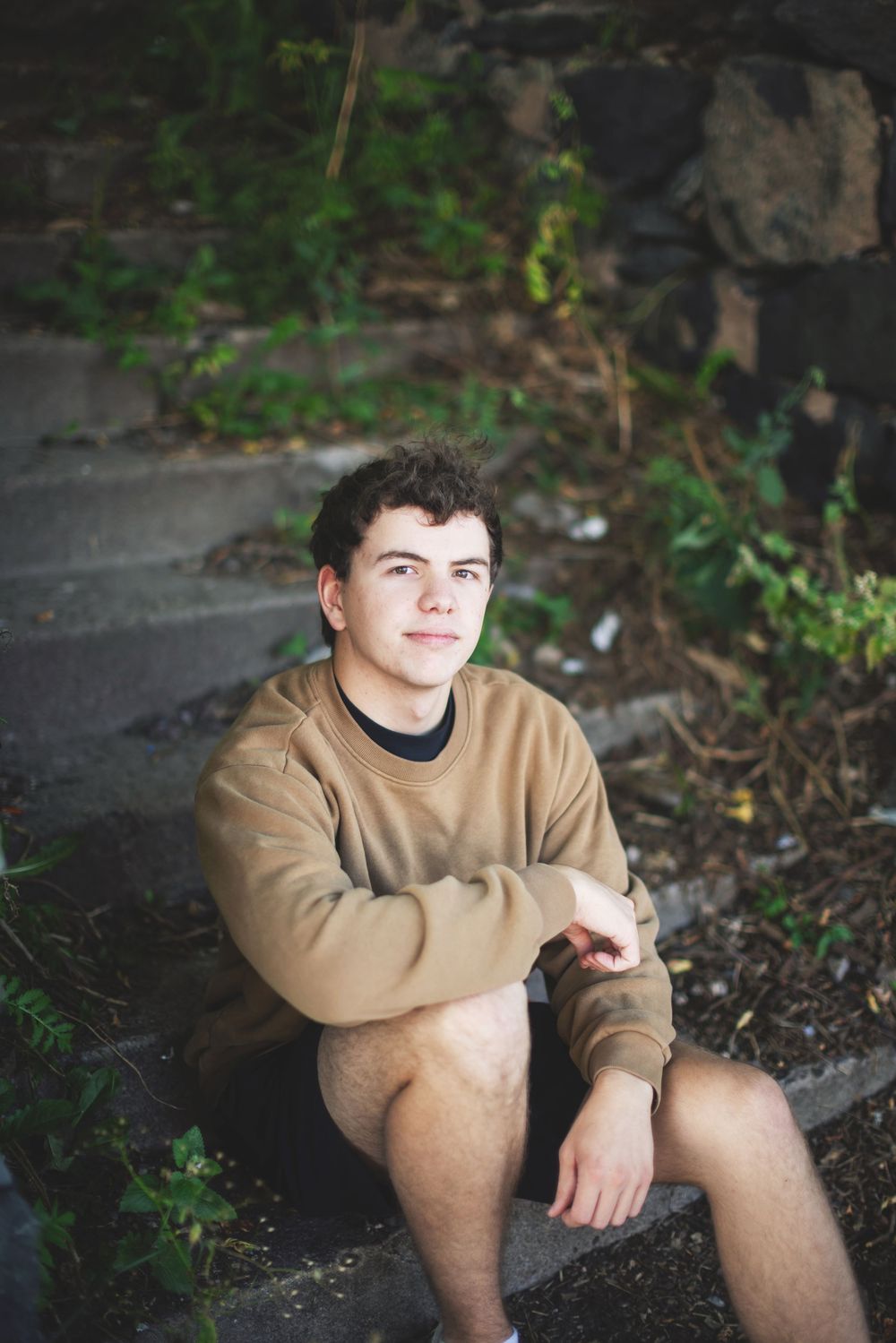 Person in beige sweater sitting outdoors against natural backdrop with greenery.