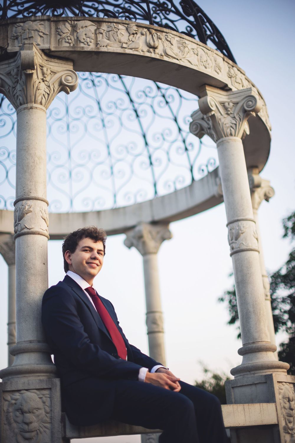 A decorative white stone gazebo with ornate columns and architectural details of a senior photography session