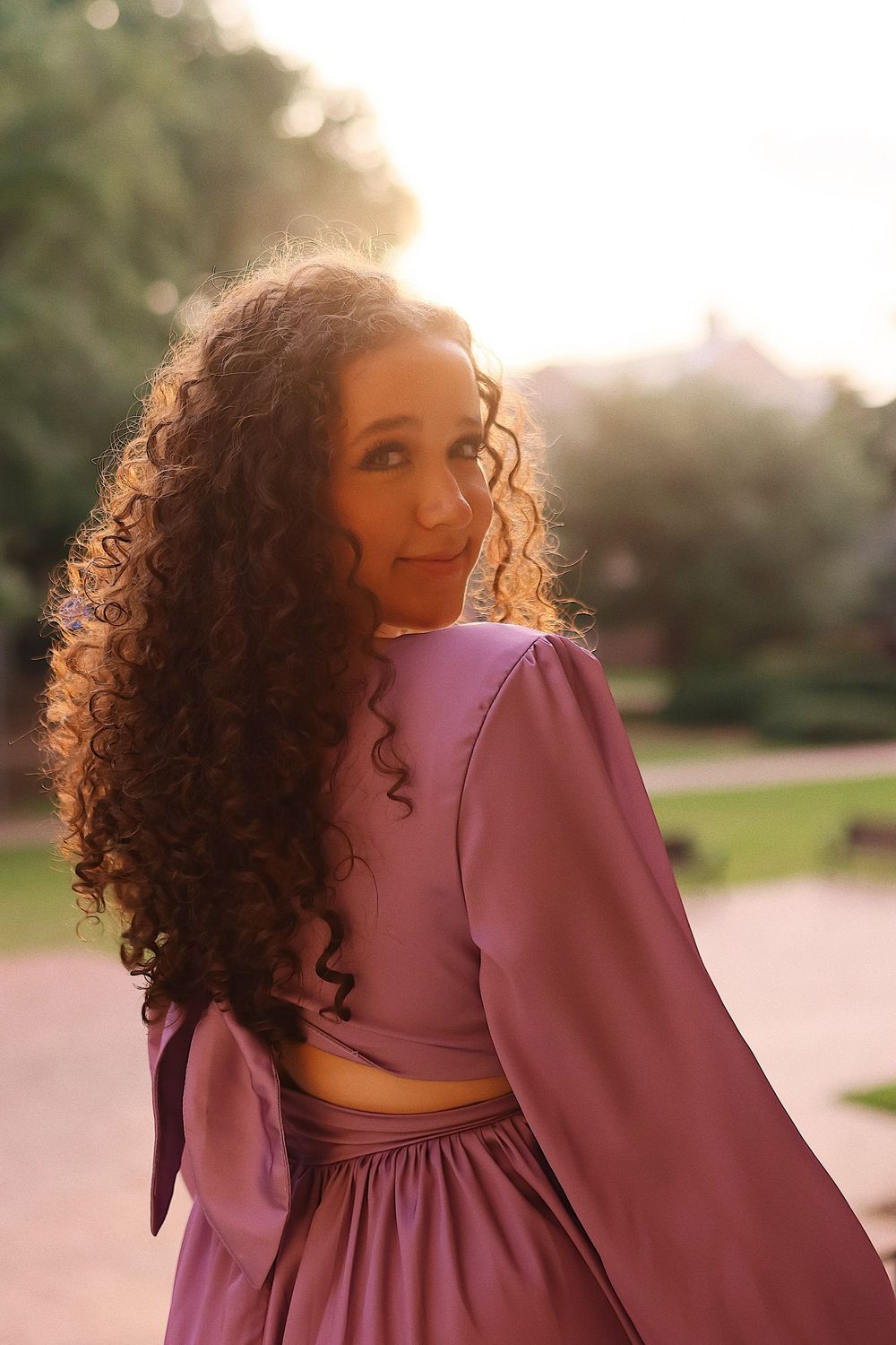 A person in a plum-colored dress poses against a sunlit outdoor background in a series of connected photos.