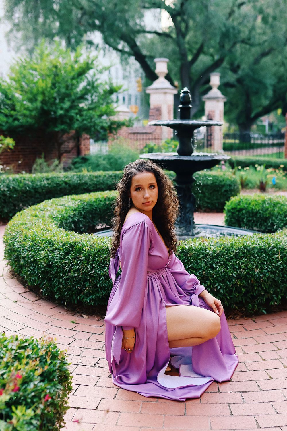 A series of outdoor portrait photos featuring someone in a flowing lilac dress posing on brick pavement near manicured hedges.