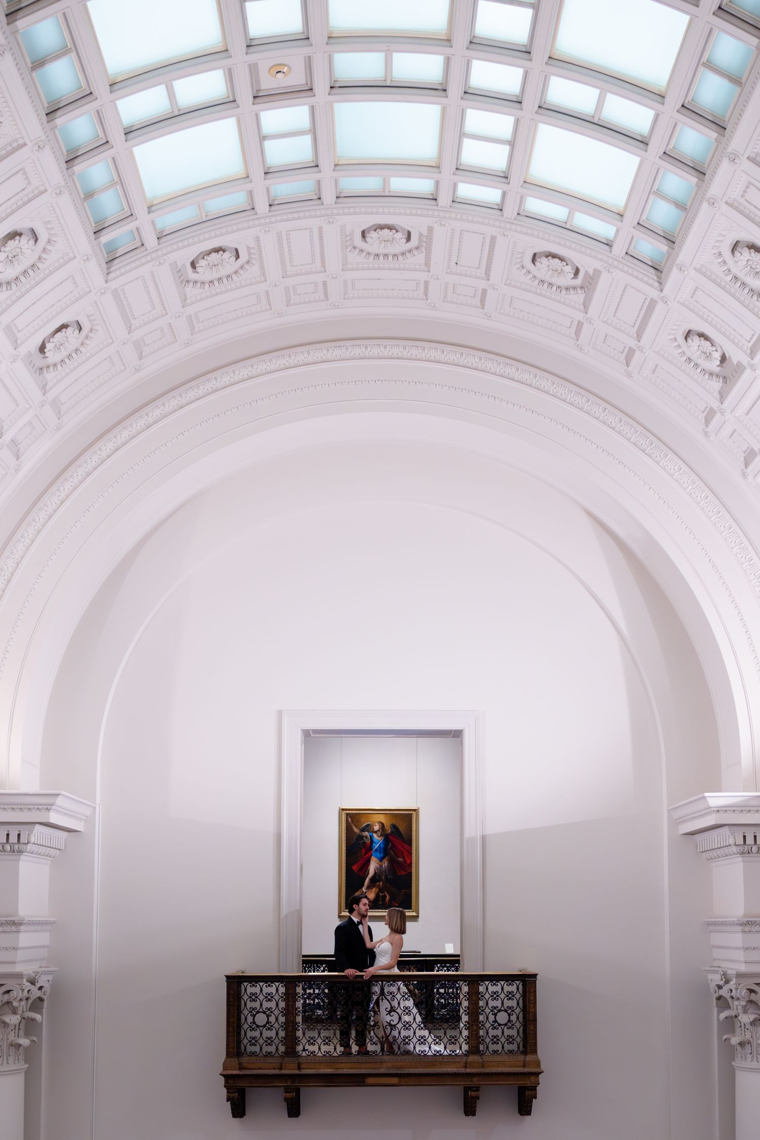 Architectural detail of arched ceiling with skylight panels above ornate balcony and painting.