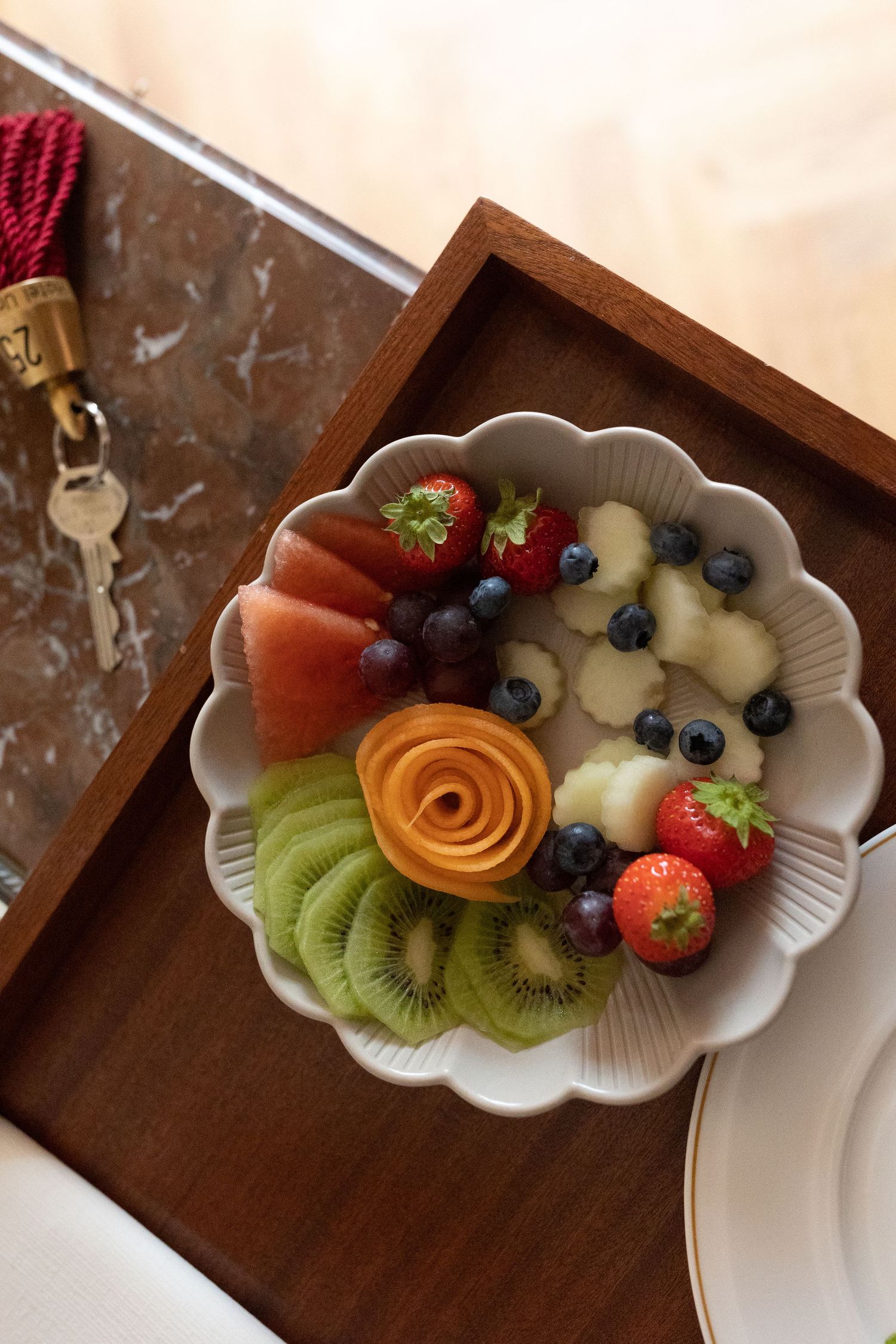 Artfully arranged fresh fruit platter with kiwi, berries and carved cantaloupe rose on white ceramic plate.