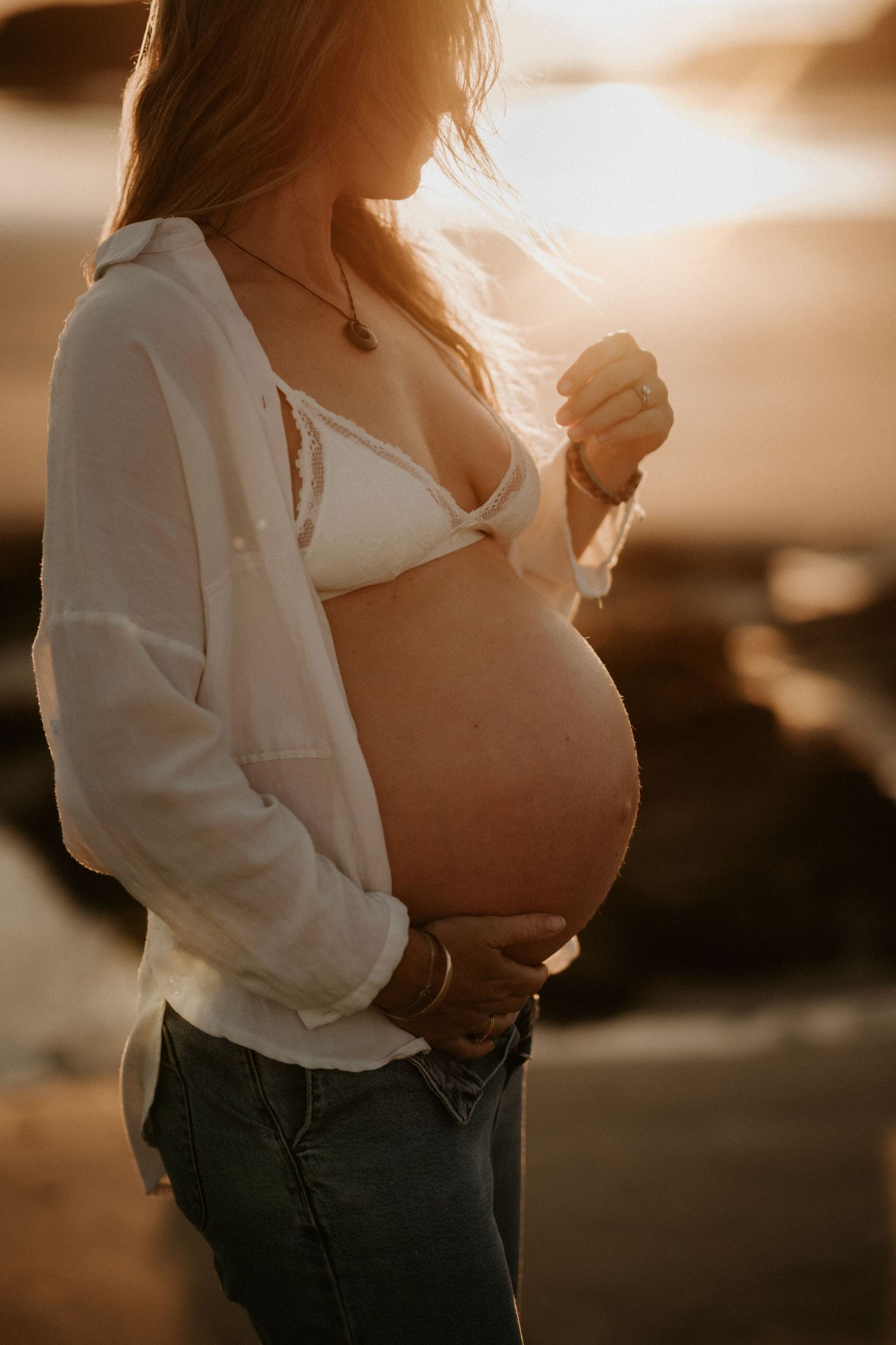 Expectant mother in golden robe posing by pampas grass in natural light.