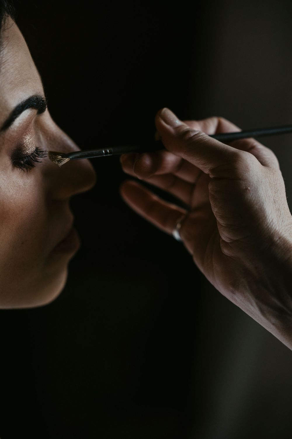 Dramatic side profile view of cosmetic application in dark lighting.