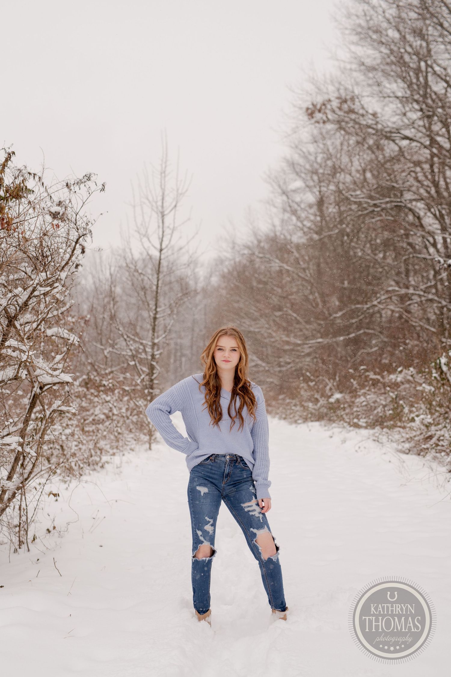Winter fashion shoot featuring distressed denim and a light blue sweater in a snowy landscape.