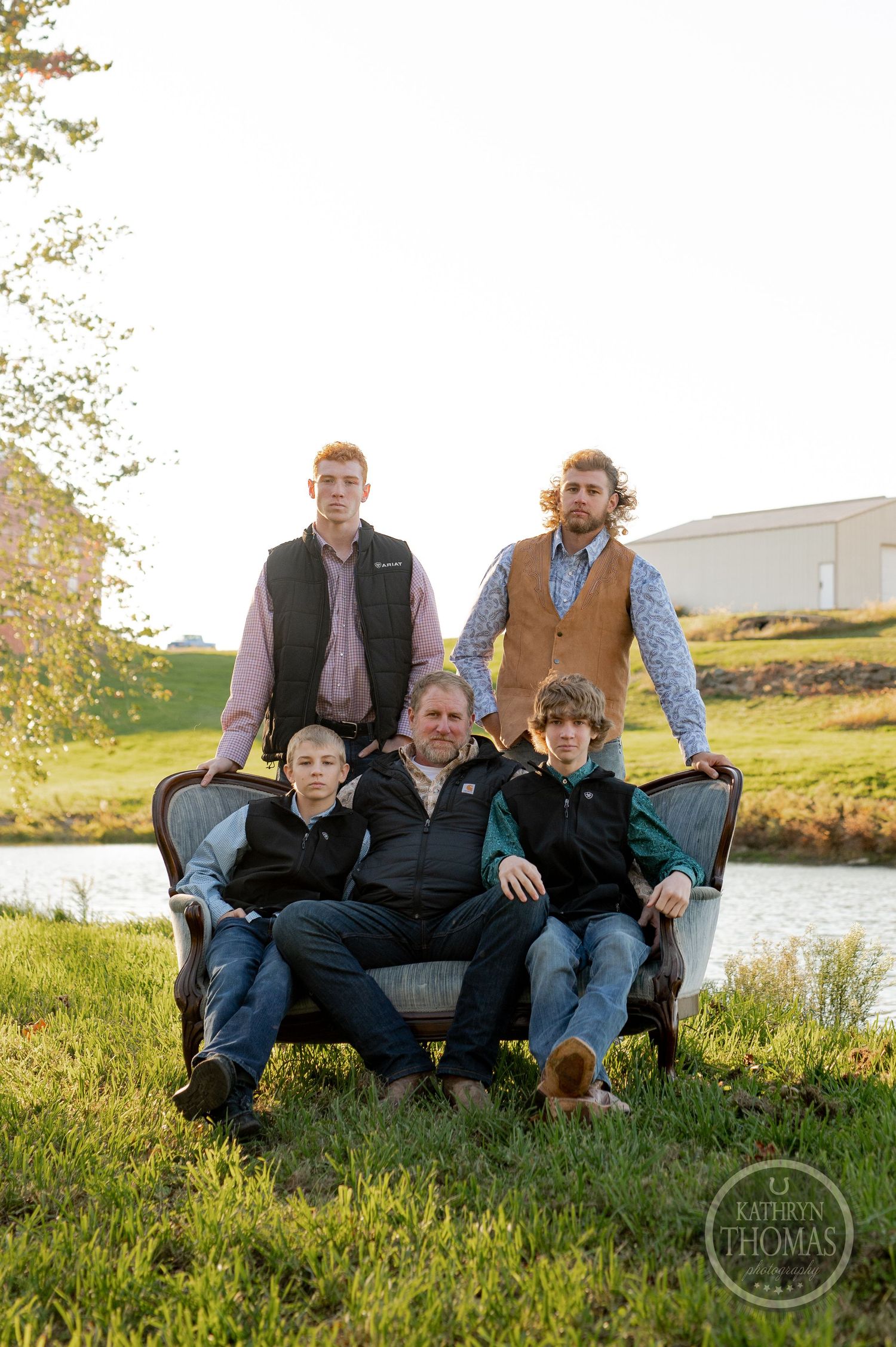 Casual group photo of family members sitting together by river during golden hour.