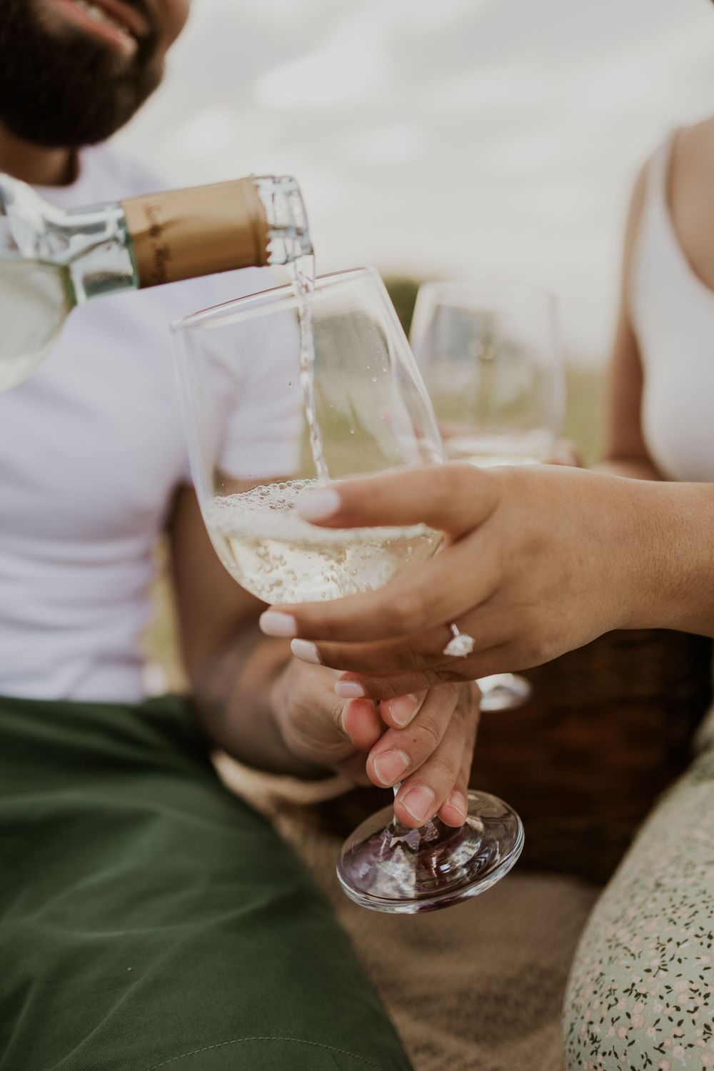 Close-up shot of white wine being poured into glass during outdoor picnic.