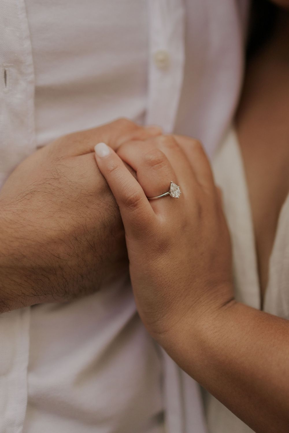 Close-up of hands with engagement ring against white shirt fabric.