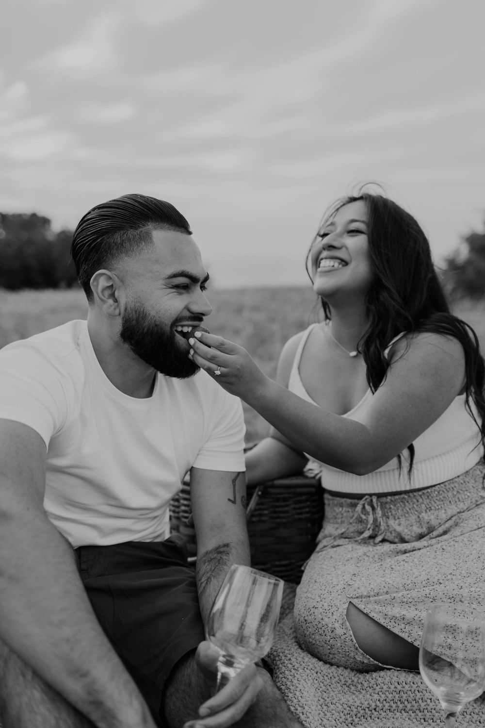 A joyful couple laughing together during a picnic in a sunny field.