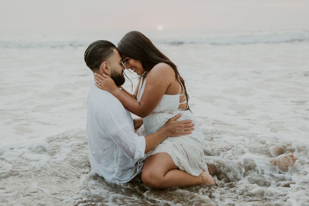 Intimate couple embracing on beach with ocean waves in background.
