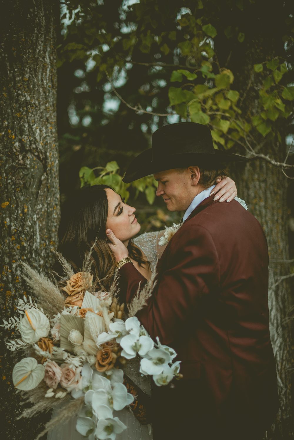 A romantic couple embraces in a forest setting while holding an elegant bouquet of white and blush flowers.