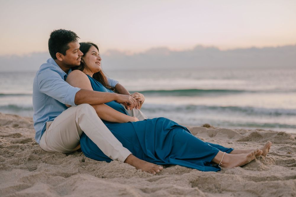 A couple sitting together on the beach at sunset with waves rolling in the background.