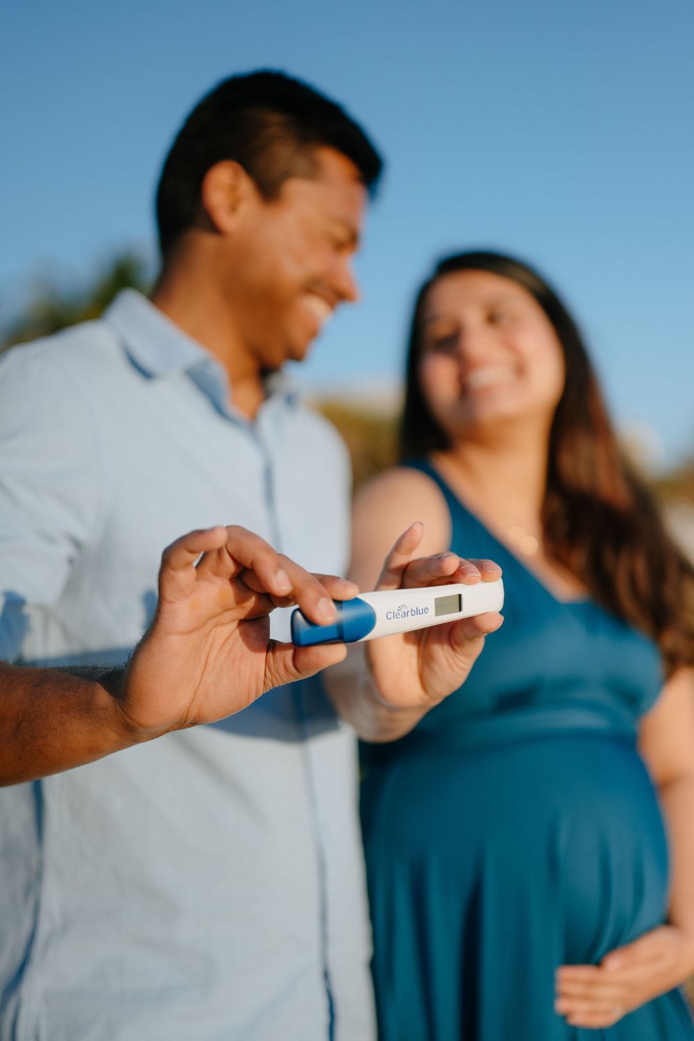 A couple showing a positive pregnancy test while standing on the beach.