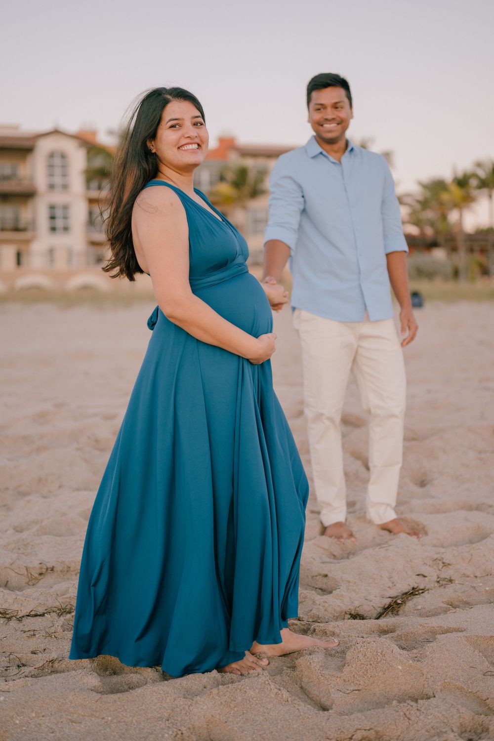 A maternity beach photo with a couple wearing coordinated outfits against a coastal backdrop.