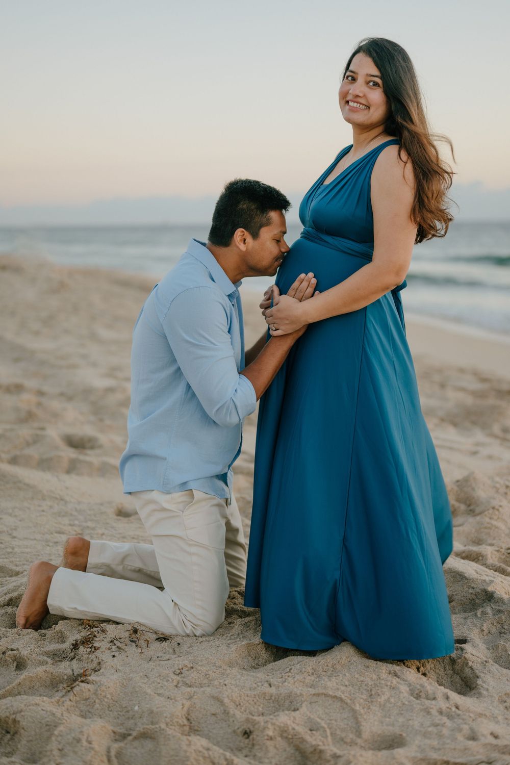 A romantic beach proposal scene with a person in a blue dress and another kneeling in the sand.