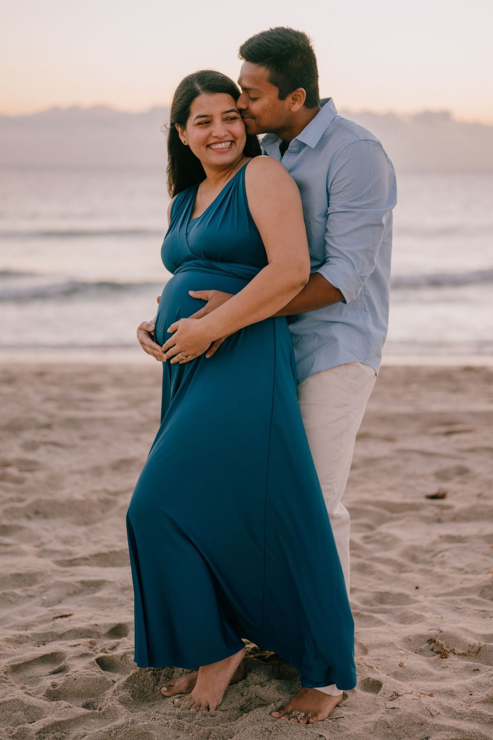 An intimate maternity photo on the beach with a couple in coordinating blue and light colored outfits.