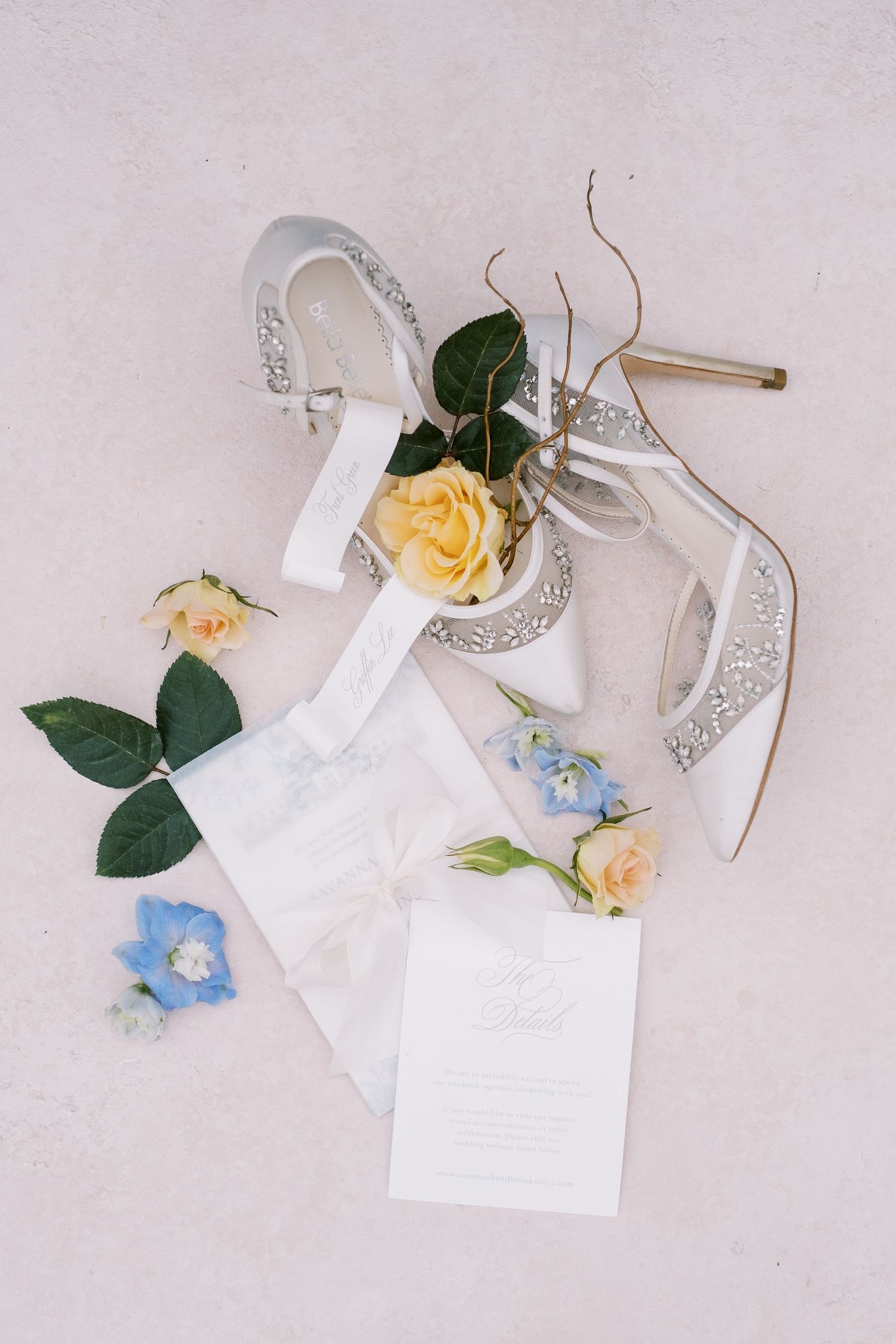 Wedding accessories including sparkly heels, roses and invitation on pink background.