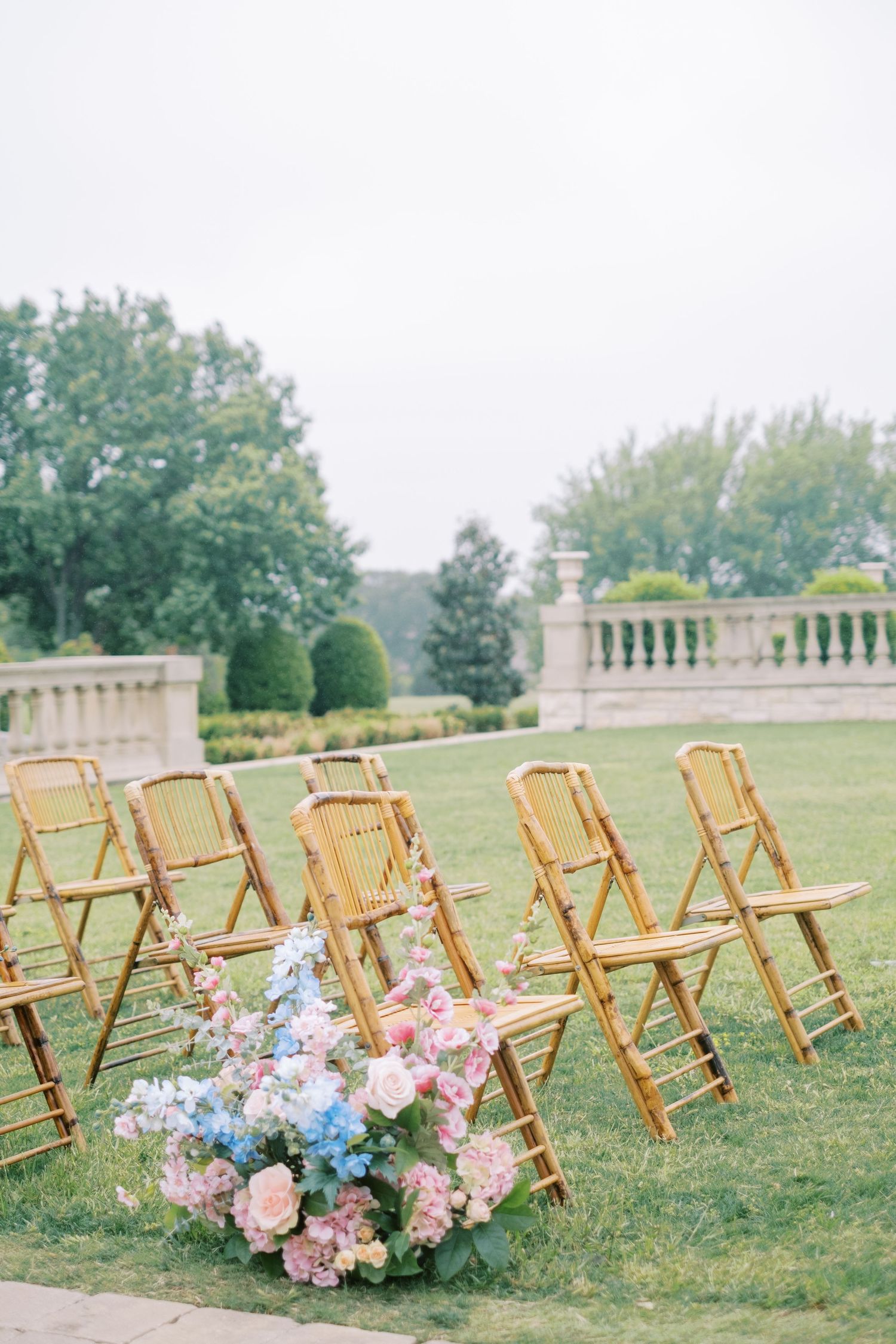Wooden folding chairs set up for outdoor ceremony with pink and blue floral arrangements.